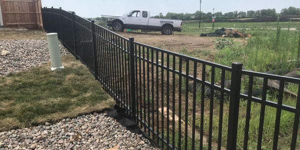 Black metal fence dividing a gravel and grass yard with a white truck in the background.