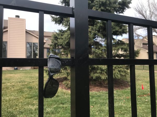 Sunglasses hanging on a black metal fence with houses and trees in the background.