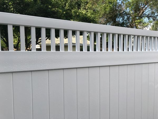 White vinyl fence with vertical slats and trees in the background.
