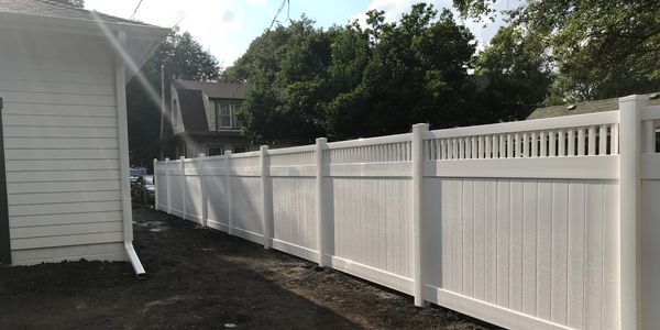 A long white vinyl fence along a house with soil on the ground.