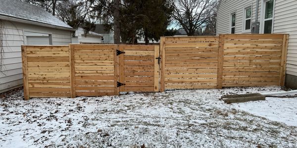 A wooden fence with a gate in a snowy backyard.