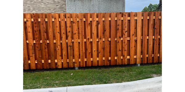 Wooden fence in front of a modern building with a grass lawn.