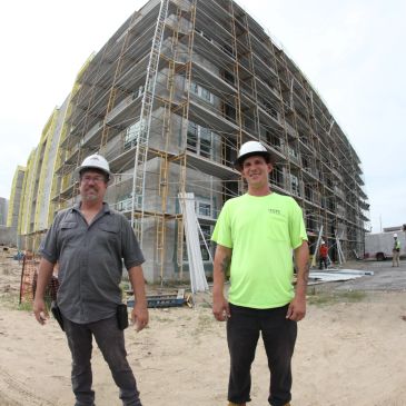 Two construction workers stand in front of a building under construction.
