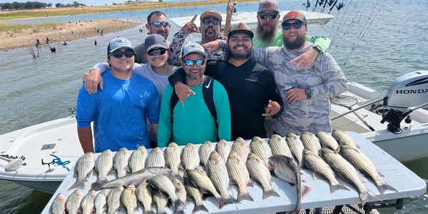 Group of men proudly displaying a large catch of striped bass by the water.