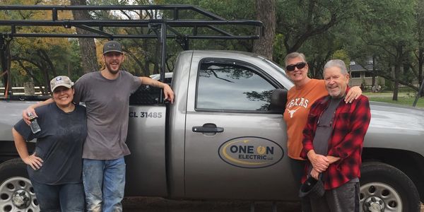 Four people smiling and posing by a One On Electric company truck outdoors.