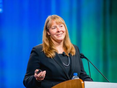 Woman speaker confidently addressing audience at a podium.
