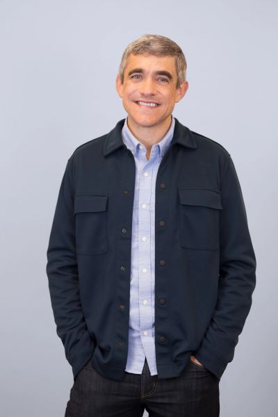 Smiling man with hands in pockets against a light background.