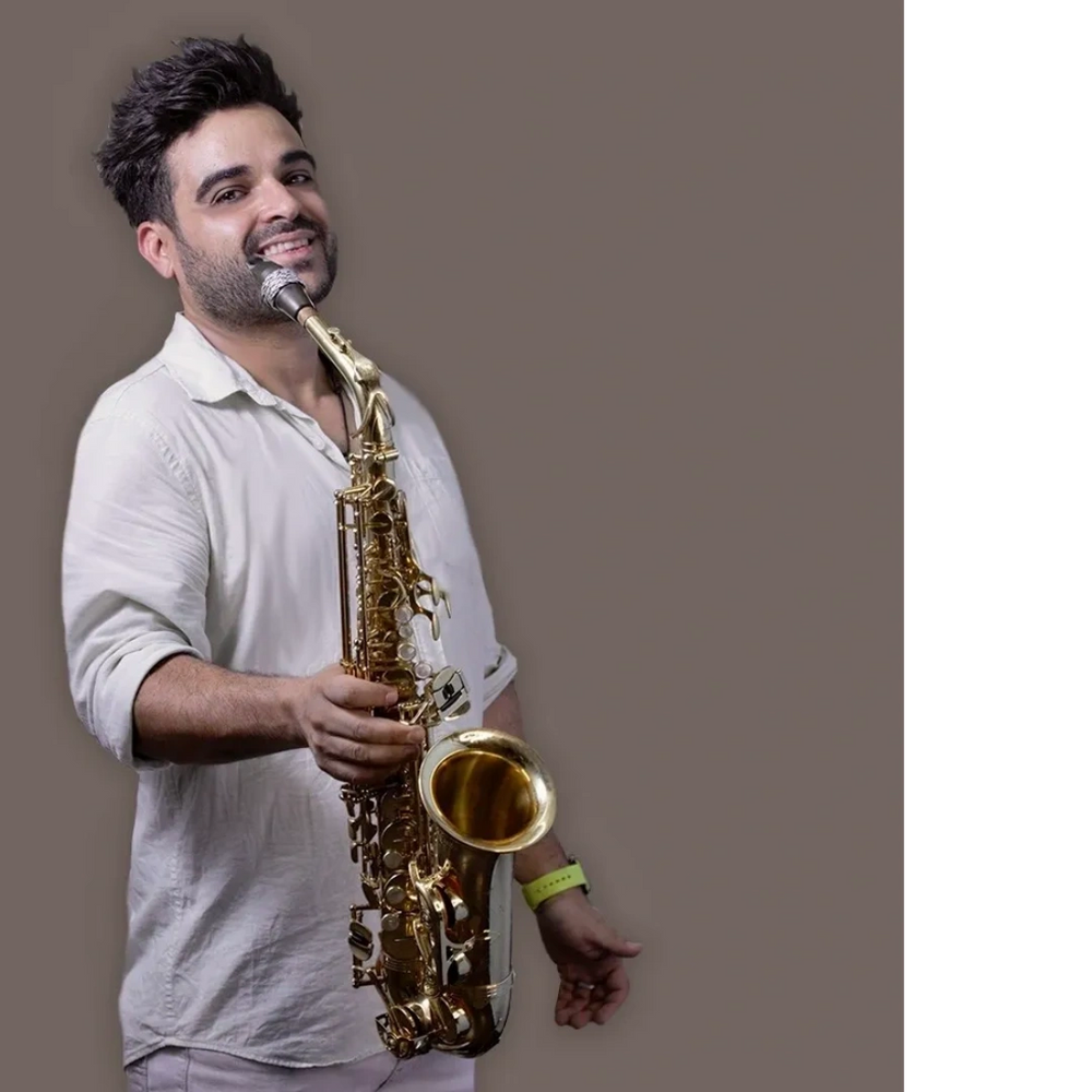 Man smiling while holding a saxophone against a plain background.
