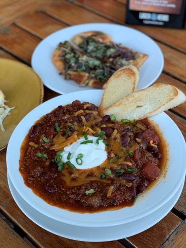 Bowl of chili topped with cheese, sour cream, and green onions, served with two slices of toasted bread.