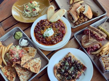 A variety of dishes including chili, quesadillas, sandwiches, and fries on a wooden table.