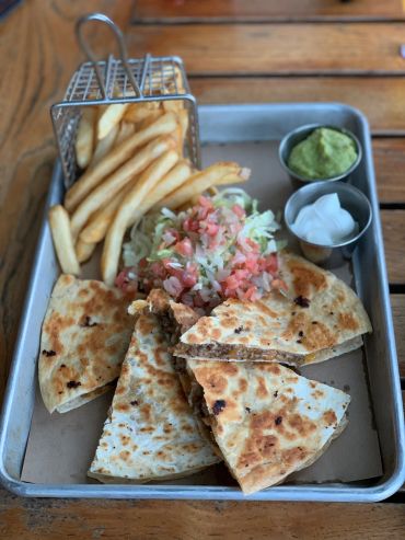 Quesadillas with French fries, guacamole, and onions on a tray.