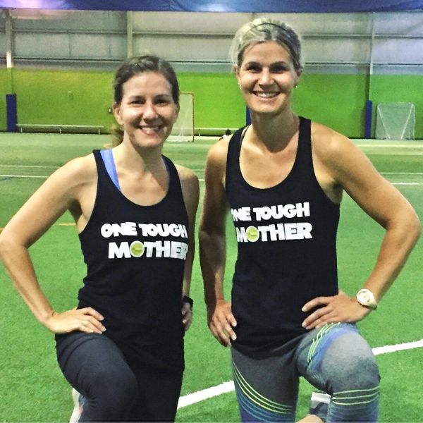 Two women in matching sports tank tops posing on an indoor turf field.