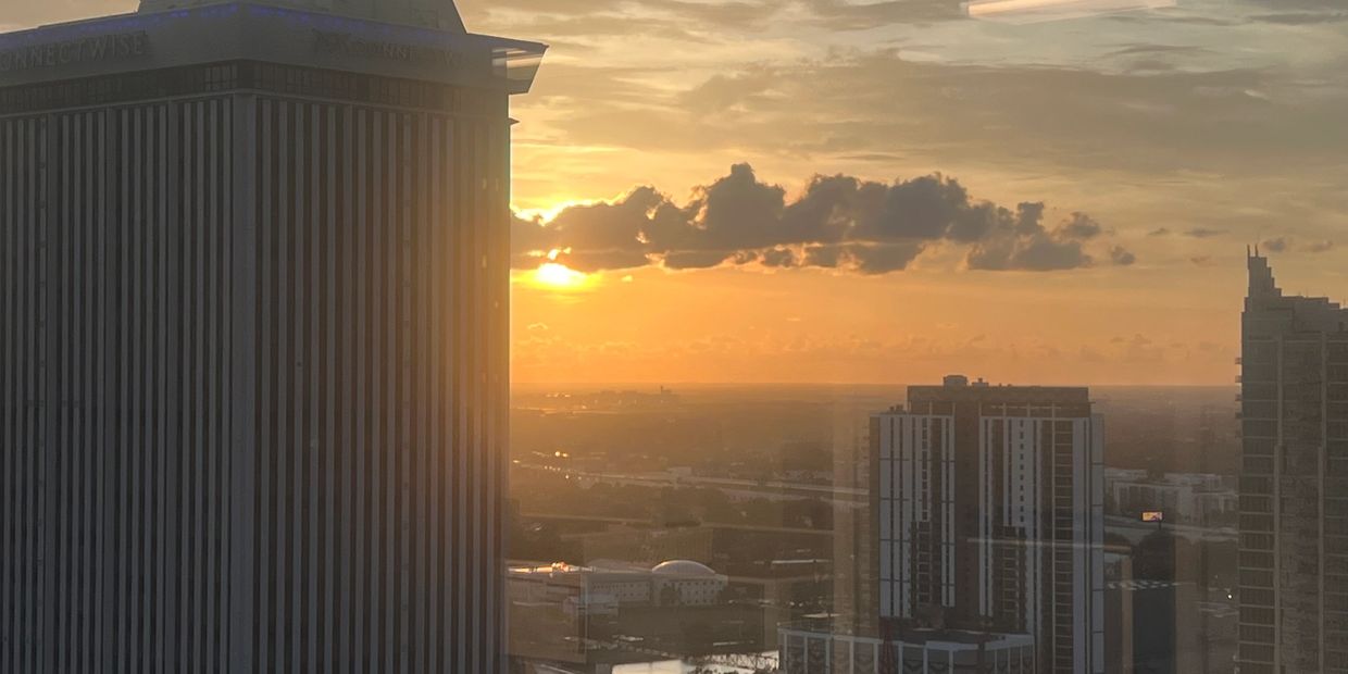 Sunset over a cityscape with tall buildings and a partly cloudy sky.