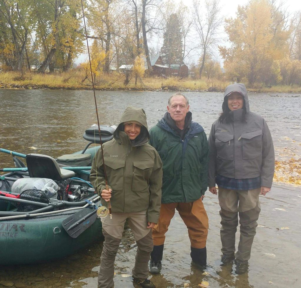 Three people in fishing gear standing in a river next to an inflatable raft.