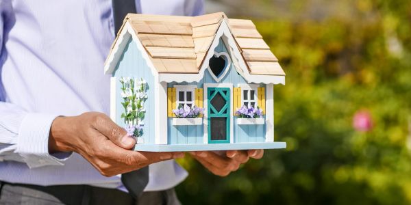 A person holding a charming miniature model house outdoors.