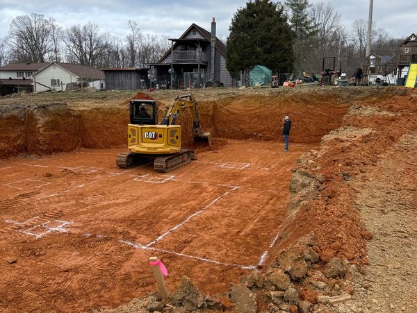 Excavation site with a yellow CAT excavator and a person standing inside the marked area.