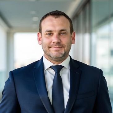 Confident man in a navy suit and tie standing indoors.