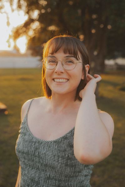 Smiling woman with glasses in a sunlit outdoor setting.