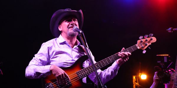 Musician playing bass guitar and singing on stage.