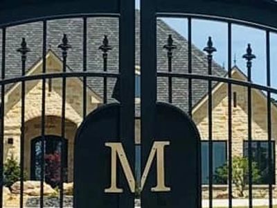 Elegant black iron gate with a large letter M in front of a stone house.