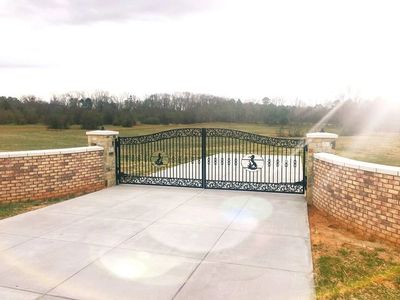 Decorative black iron gate at driveway entrance with brick pillars and walls.