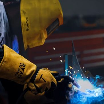 Worker welding metal with protective gear and sparks flying.