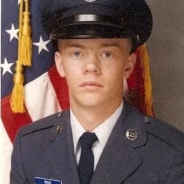 Young man in military uniform posing for a formal photo with American flag background.