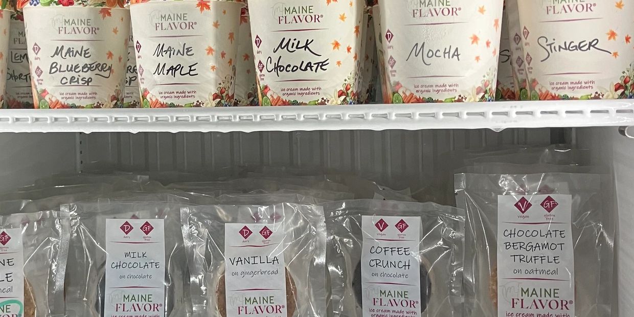 Ice cream sandwiches are displayed in a retail freezer. The shelf above shows various ice cream pint