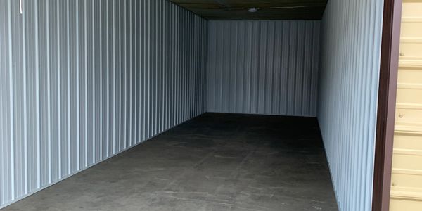 Empty metal storage unit with concrete floor and corrugated walls.