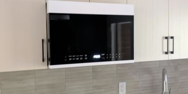 Modern microwave oven installed above kitchen countertop with white cabinets.