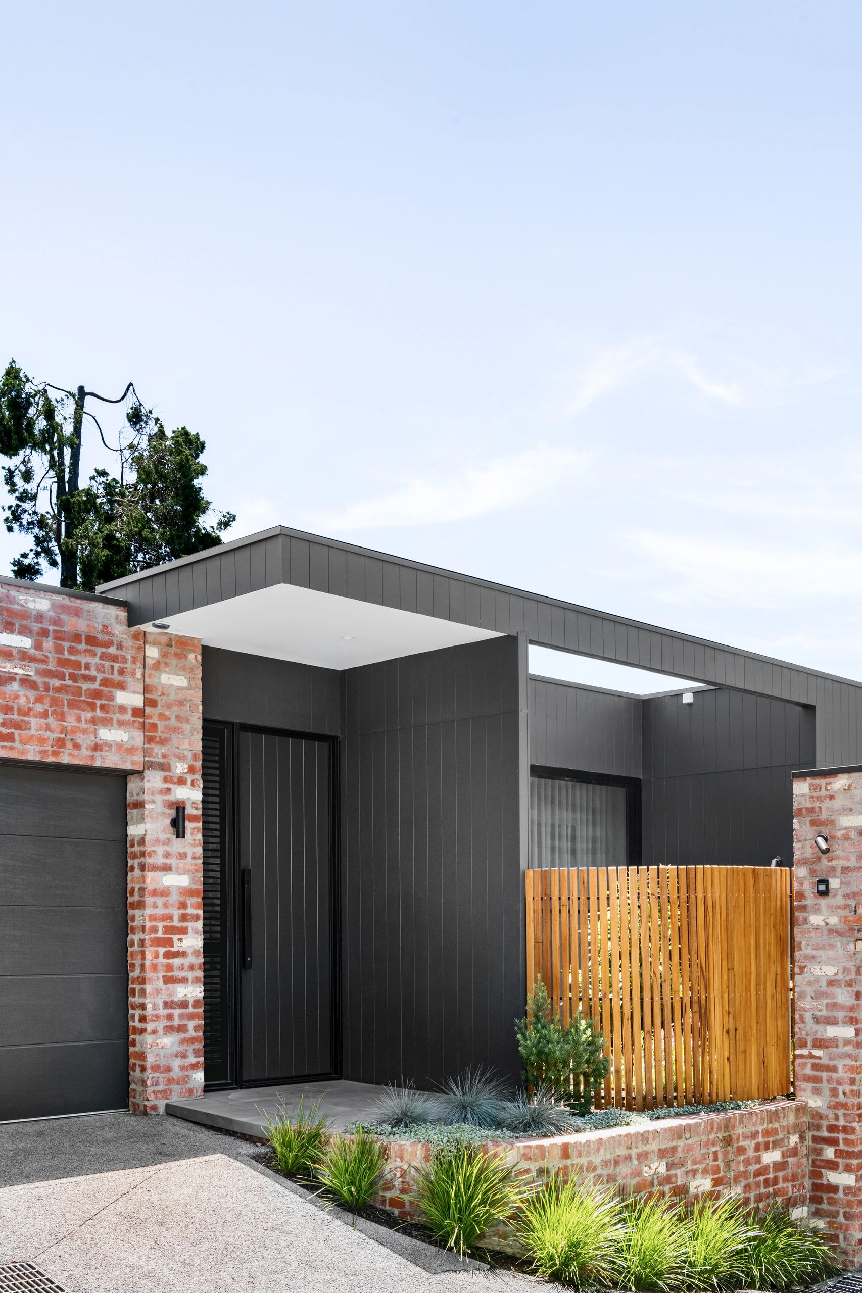 Modern house entrance with black panels, brick accents, and wooden fence.