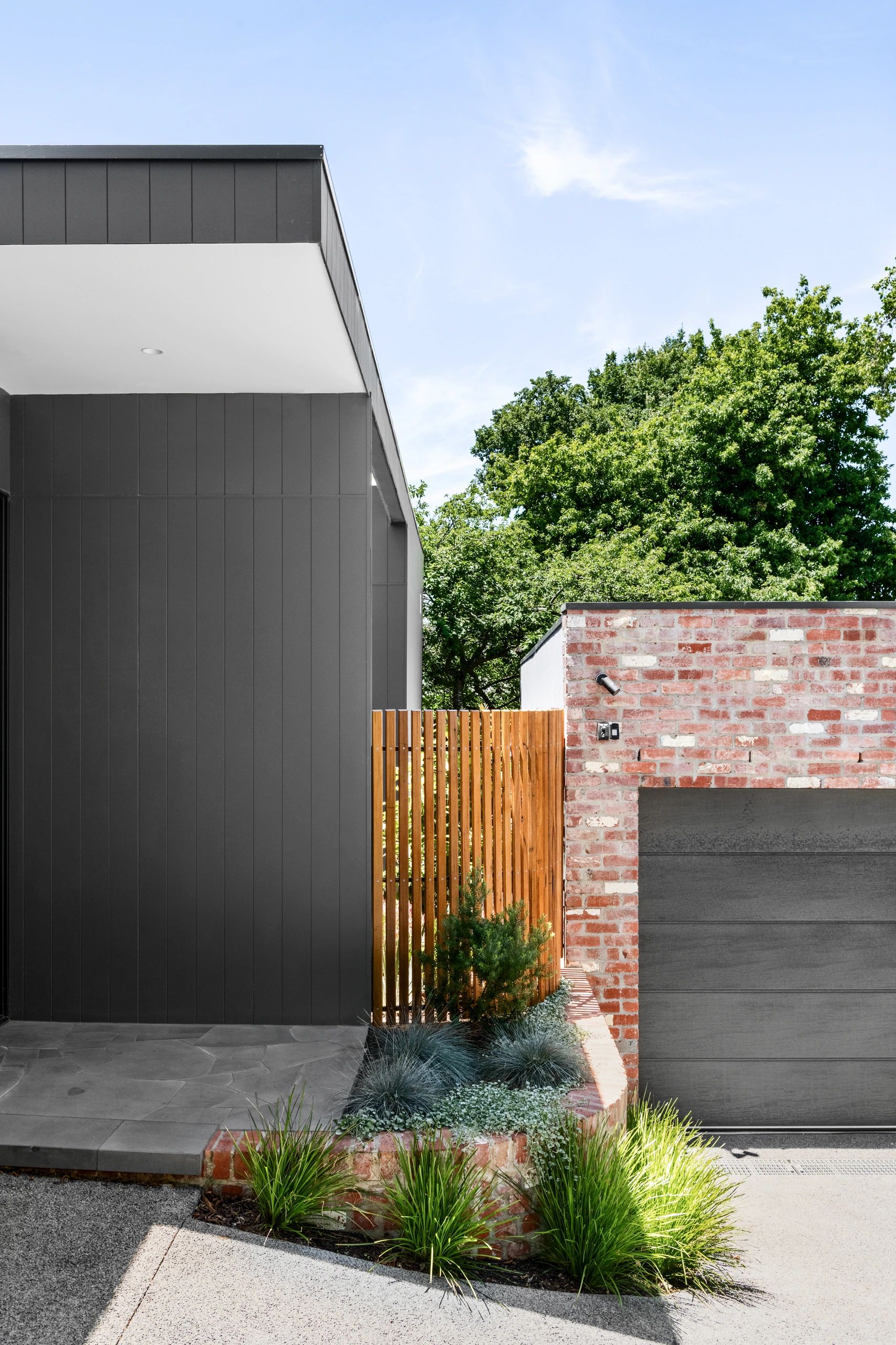 Modern home exterior with dark gray siding and brick garage.