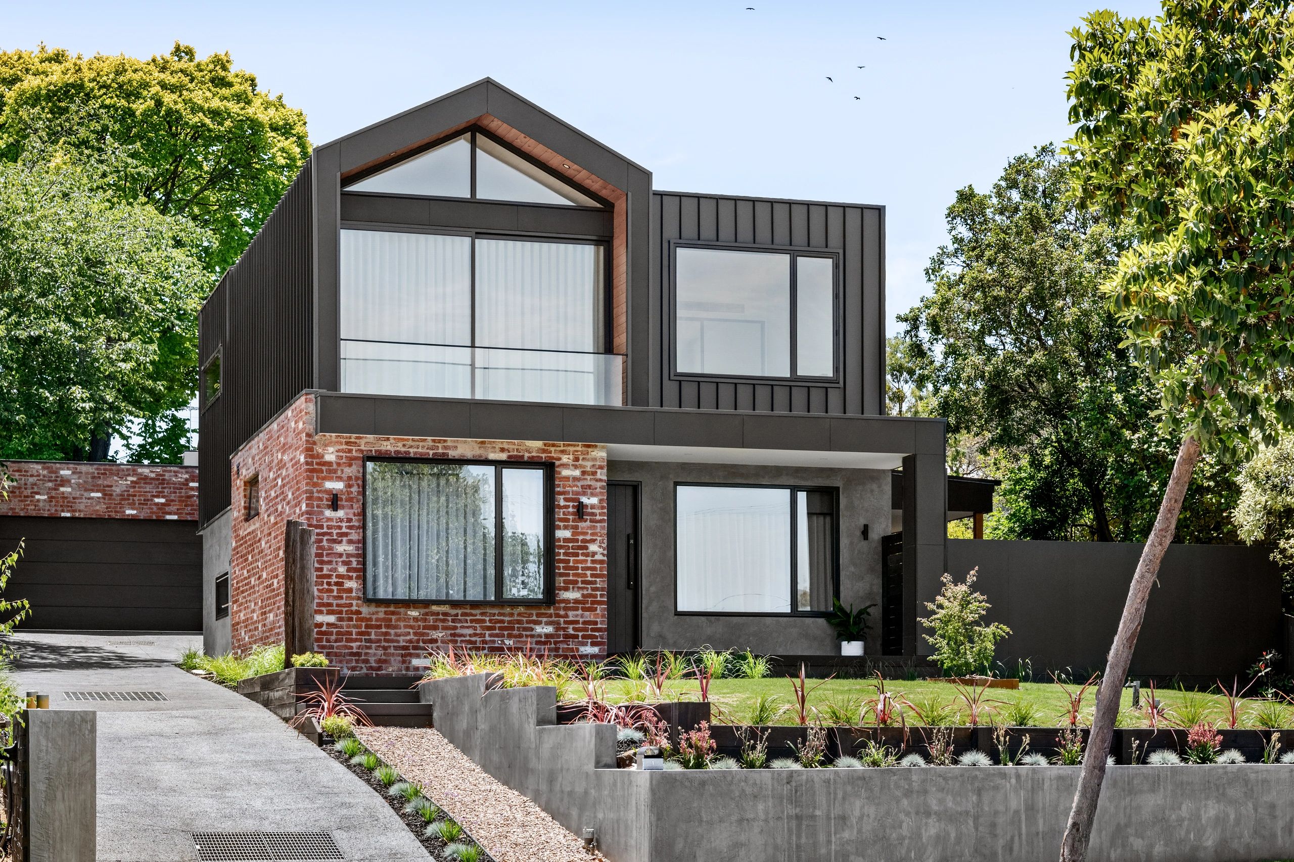 Modern house with brick and dark panel exterior, large windows, and landscaped garden.