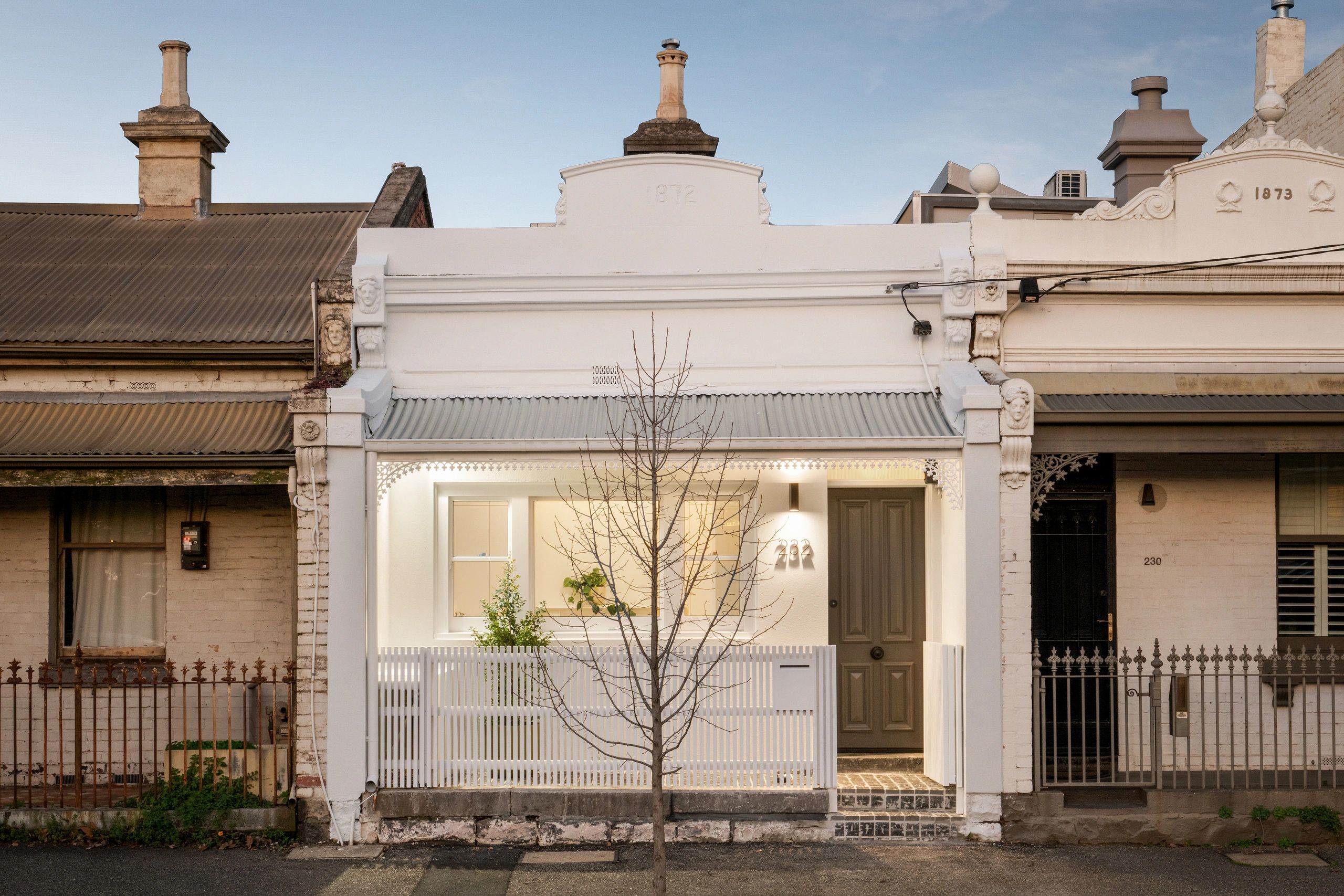 Historic row houses with white-painted facade and tree.
