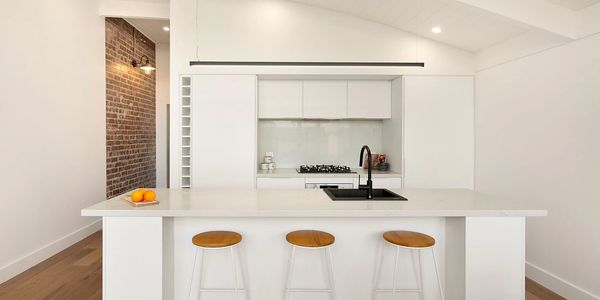 Clean white renovated modern kitchen, curved sloped roof with exposed red brick, light timber floor