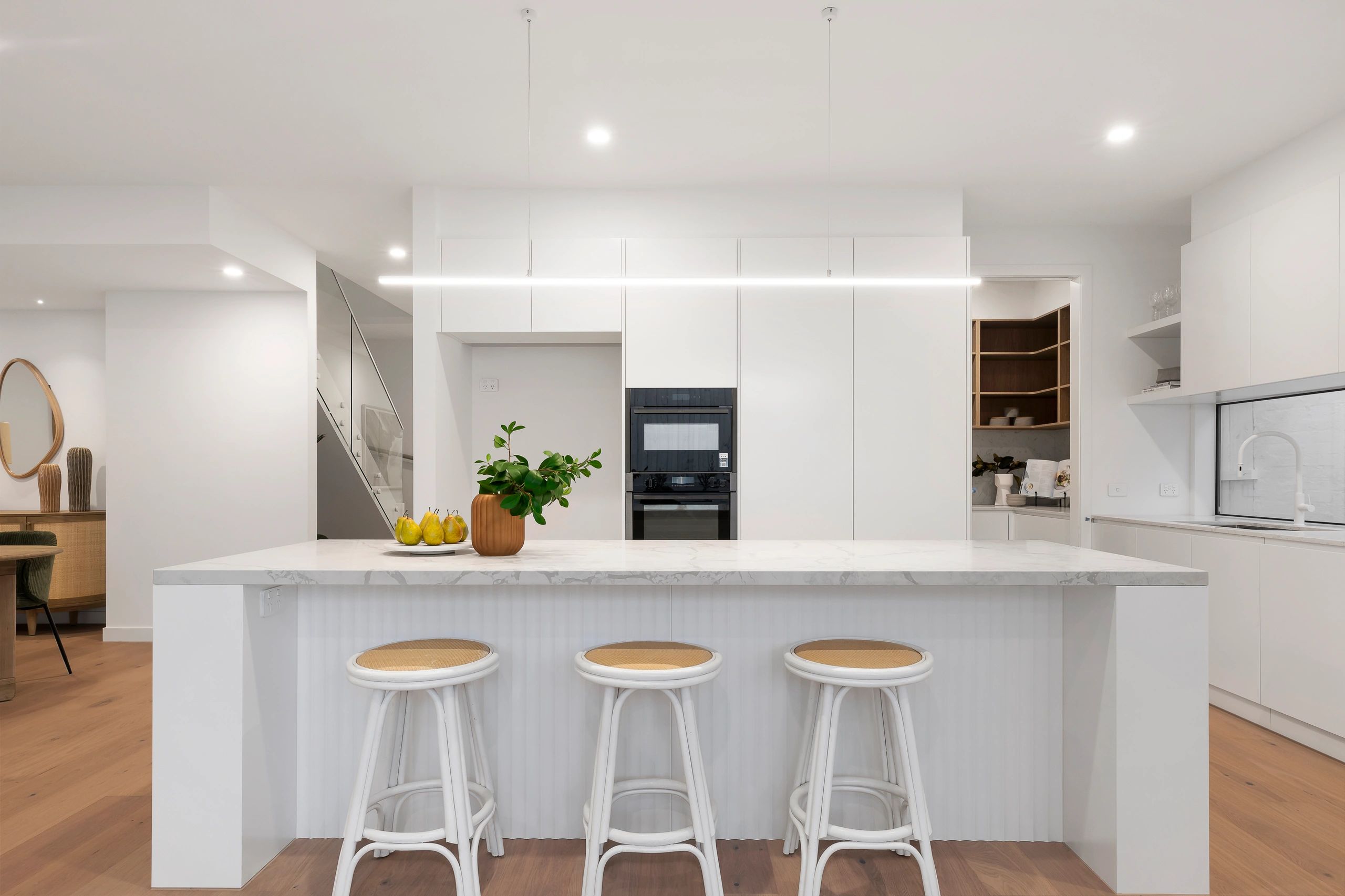 Bright white modern kitchen with marble island and stools.