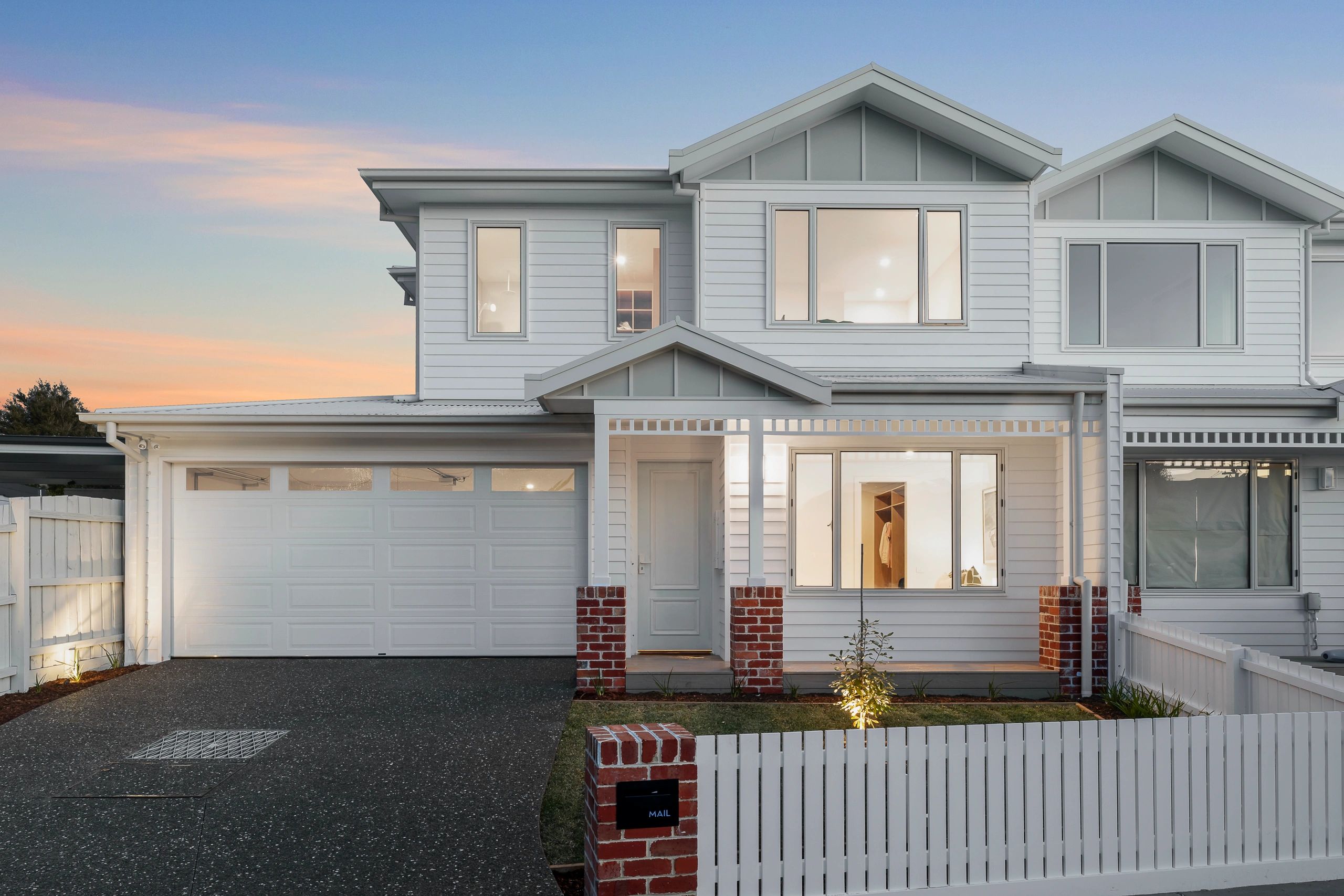 Modern two-story white house with a garage and a picket fence.