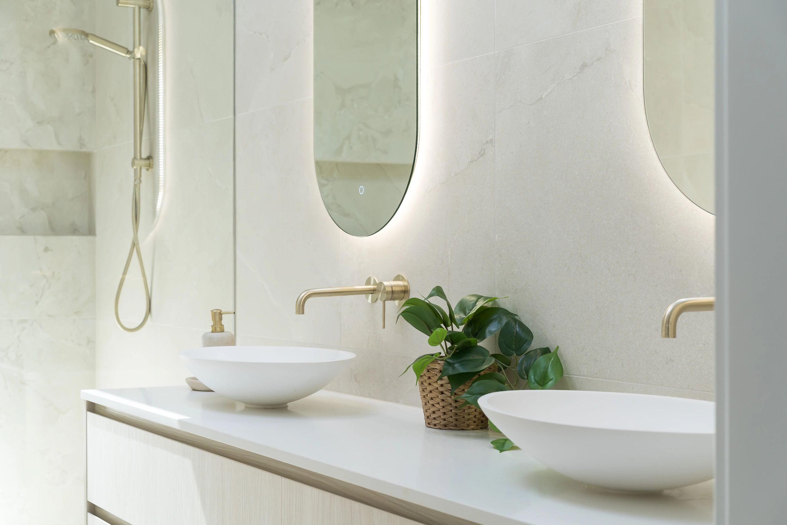 Modern bathroom with backlit mirror and gold fixtures.