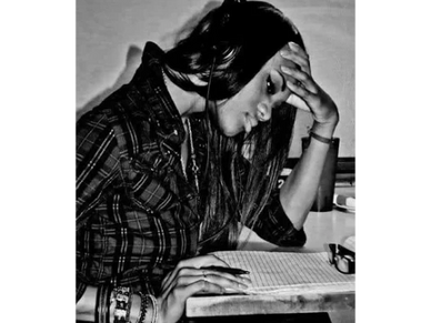 A woman deeply focused on writing at a desk in black and white.