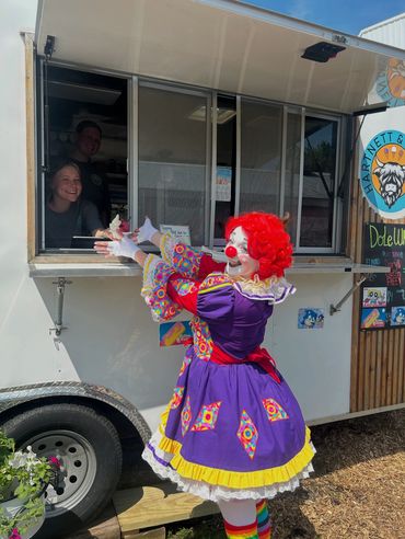 A woman giving ice cream to a girl dressed as a clown