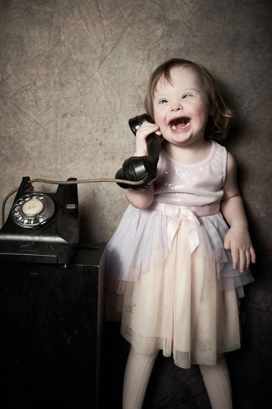 Little girl with Down syndrome smiling whilst answering a telephone. 
