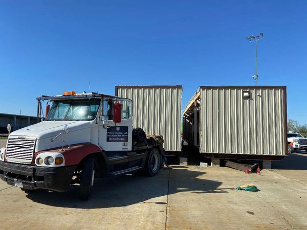 Truck parked next to two large mobile home sections under a clear blue sky.