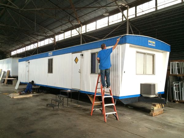 Two men working on a mobile home inside a large warehouse.