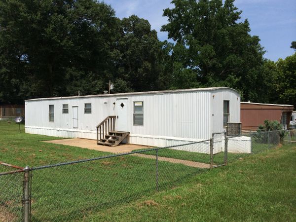 White mobile home with small stairs and a fenced yard on a sunny day.