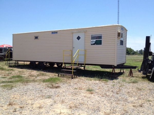 A beige mobile trailer on a grassy lot with metal stairs leading to the door.