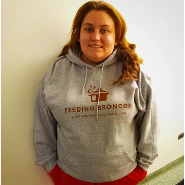 Person wearing a gray hoodie with "Feeding Broncos" text and red pants.