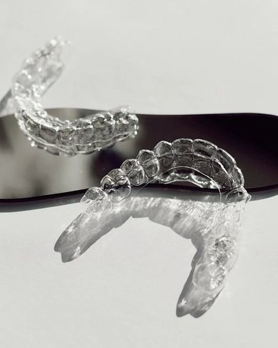 Clear dental aligners casting shadows on a reflective surface.