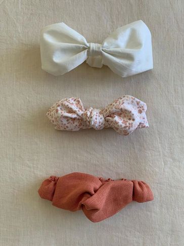 Three fabric hair bows in white, floral, and terracotta colors on a beige background.