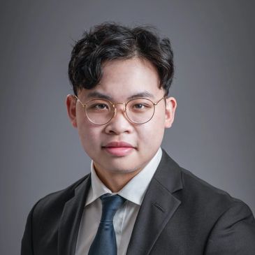 Young man in glasses wearing a suit and tie against a gray background.