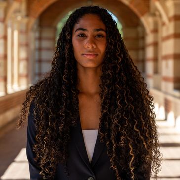 Confident woman with long curly hair standing in an arched corridor.
